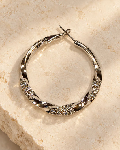 Single silver rhinestone twisted hoop resting on a stone surface