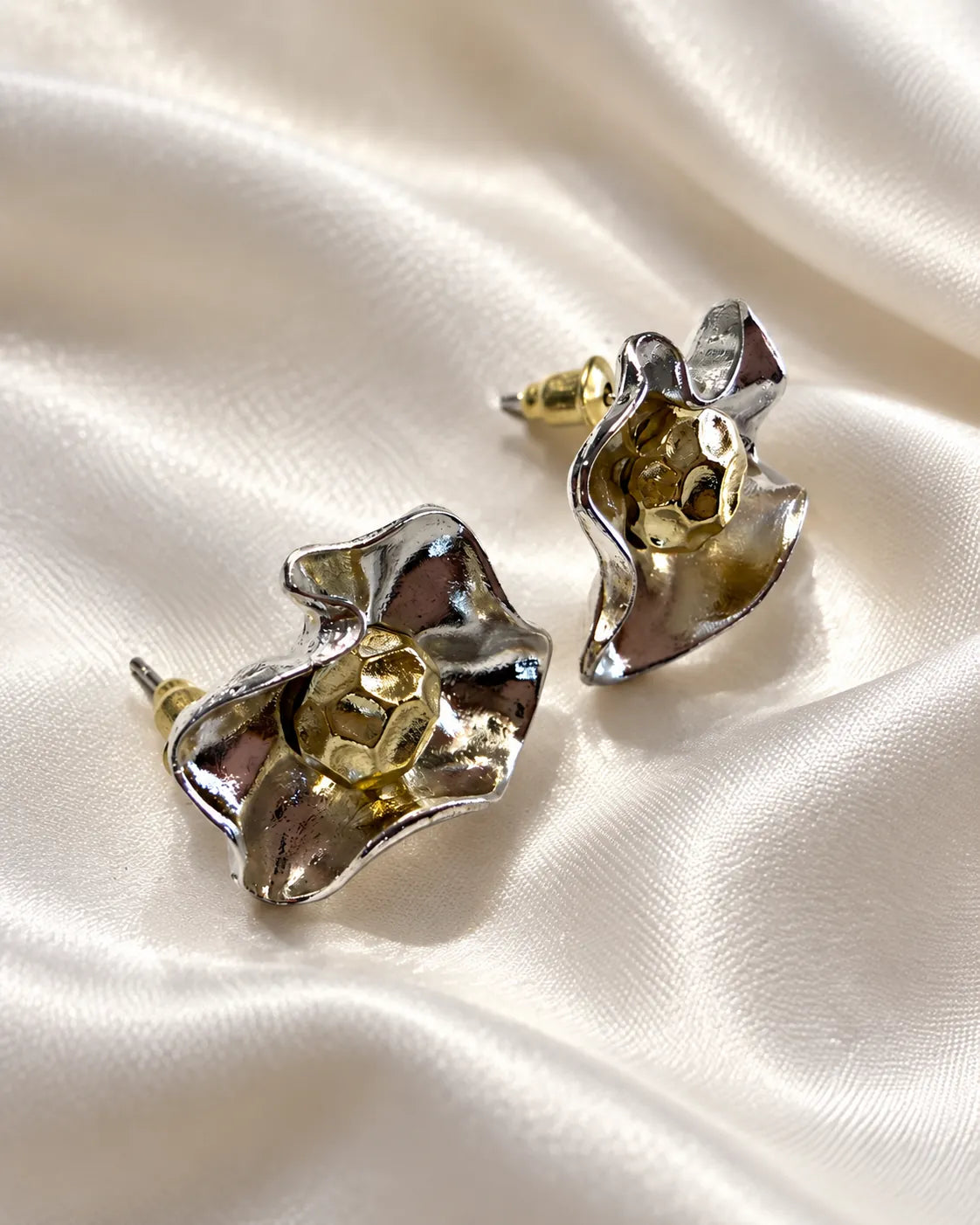 Two-tone metal flower studs resting on white satin