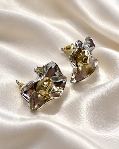 Two-tone metal flower studs resting on white satin