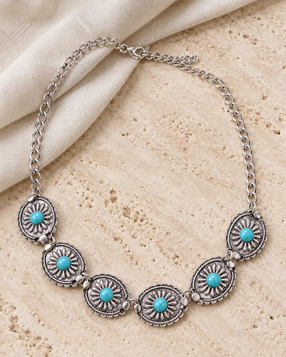 Turquoise sunburst medallion necklace laid on stone and cream linen