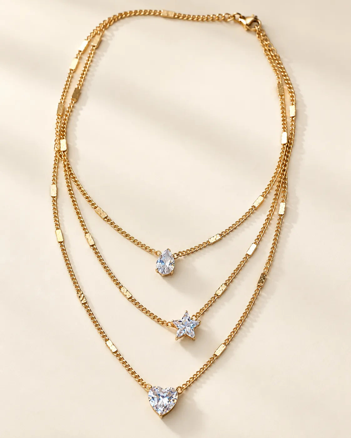 Gold three-strand crystal necklace laid flat on a cream background