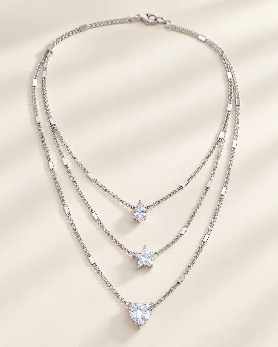 Silver three-strand crystal necklace laid flat, showing the graduated layers