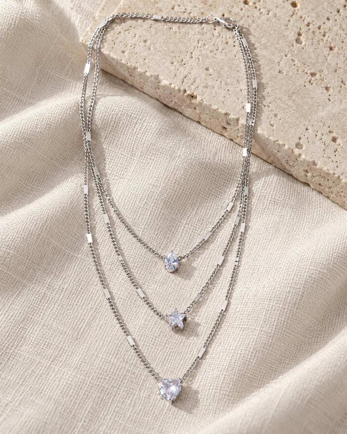 Silver trio layered necklace draped over a stone block and linen