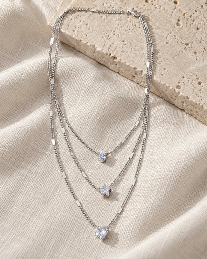 Silver trio layered necklace draped over a stone block and linen