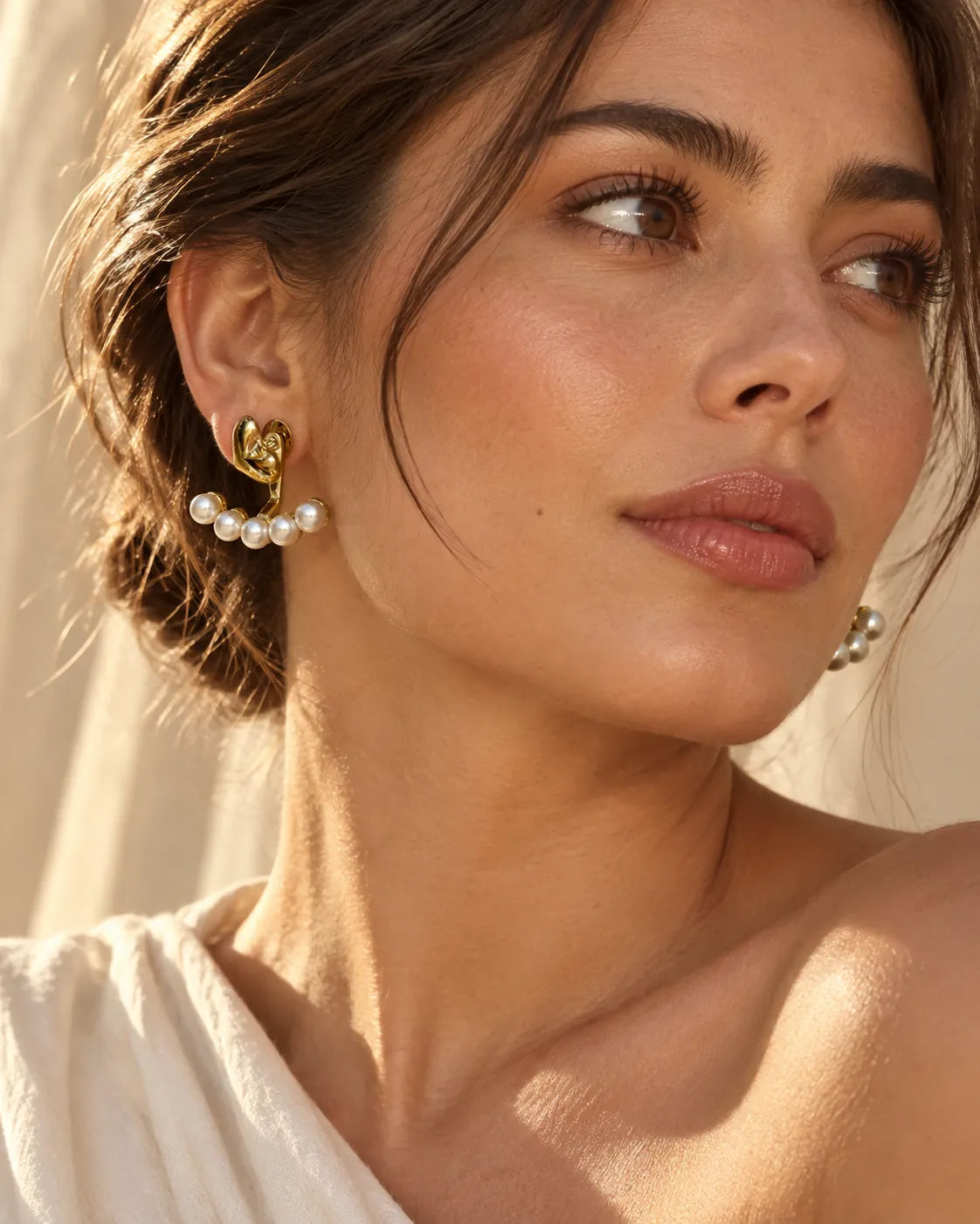 Model in a white top wearing the gold heart and pearl-look stud earrings