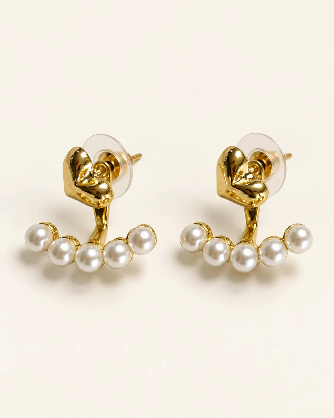 Amora gold heart knot studs with pearl-look beads on a cream background