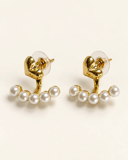 Amora gold heart knot studs with pearl-look beads on a cream background