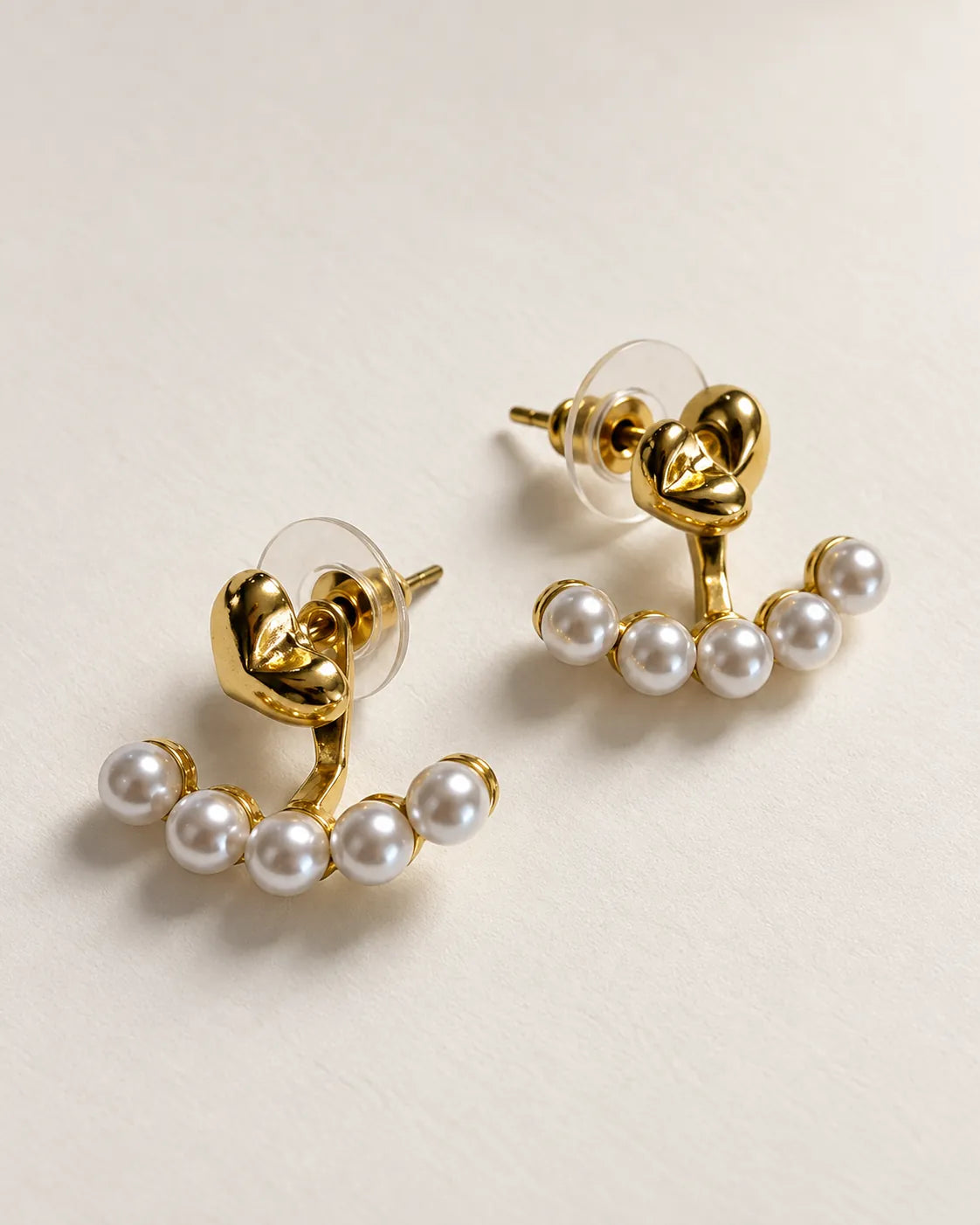 Pair of gold-tone heart and pearl-look stud earrings on a grey surface