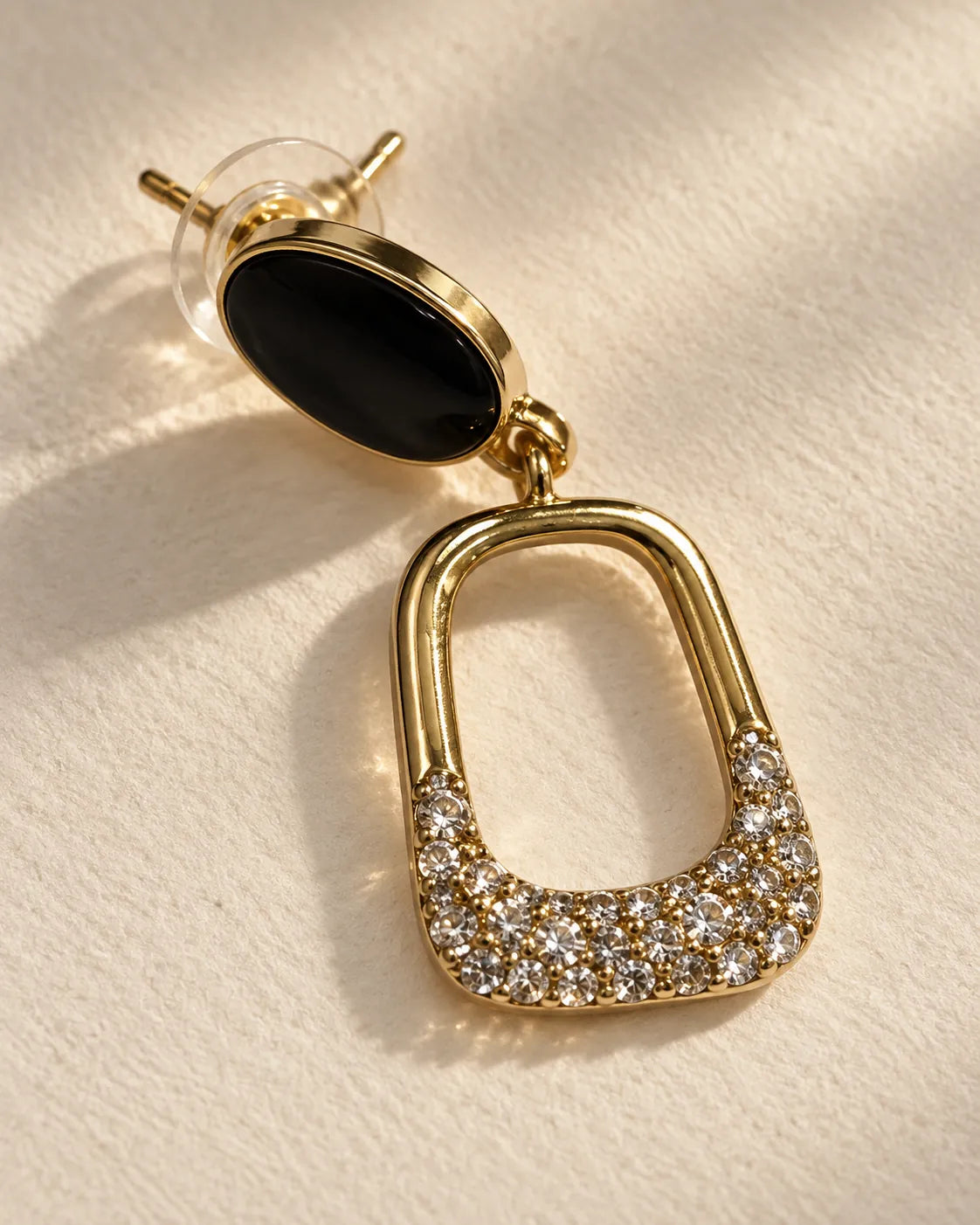 Pair of black enamel oval stud drop earrings with gold-tone open drops on cream