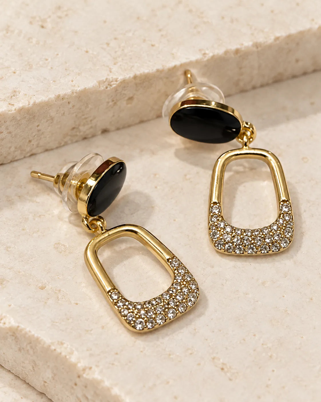 Black enamel stud drop earrings resting on a cream stone surface