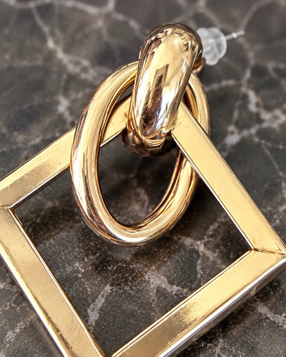 Close-up of the polished gold oval loops and square frame on dark marble