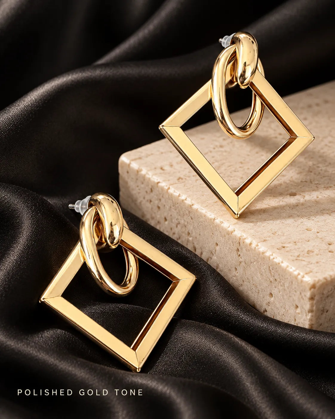 Gold-tone geometric earrings on a stone block with black satin