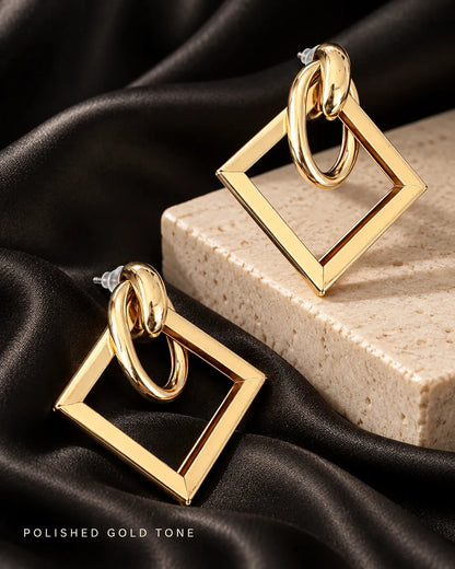Gold-tone geometric earrings on a stone block with black satin