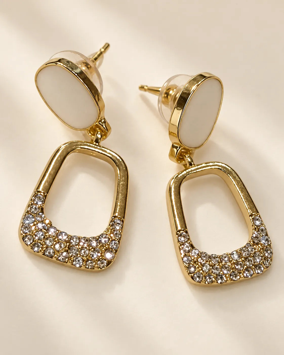 Angled view of the white oval stud drop earrings on a cream background