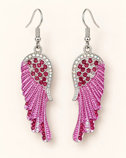 Pink enamel angel wing crystal earrings with fish-hook wires on a cream background
