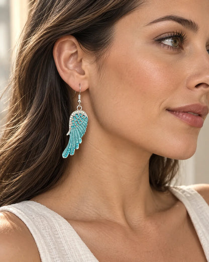 Side profile of a model in a white top wearing the turquoise wing earrings