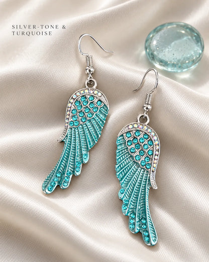 Blue angel wing earrings on white satin beside a glass accent