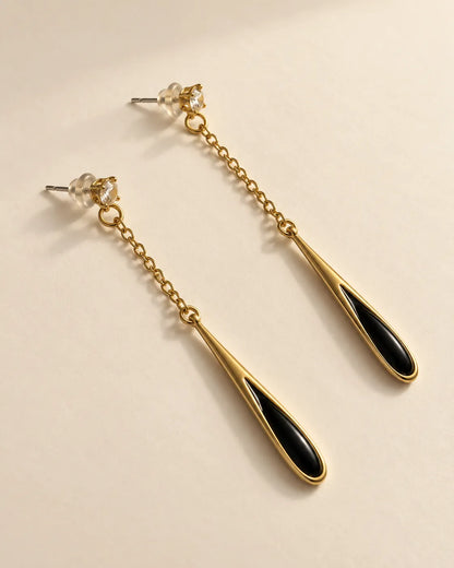 Angled view of the gold-tone chain and slim black enamel teardrop earrings