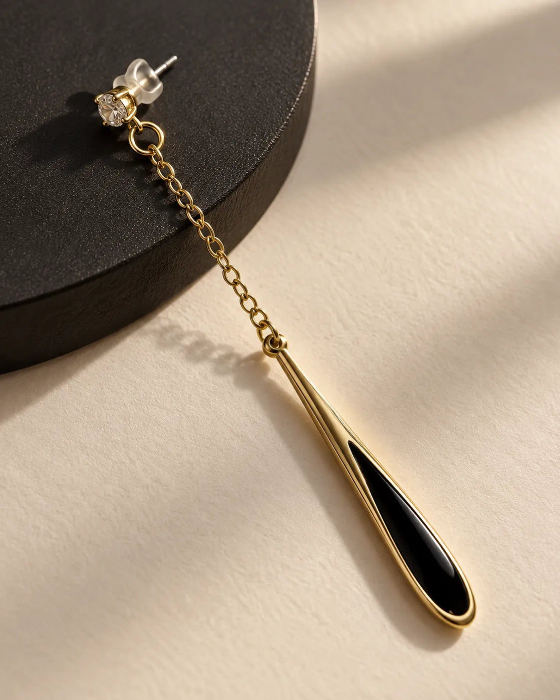 Single black teardrop chain earring on a dark surface in sunlight