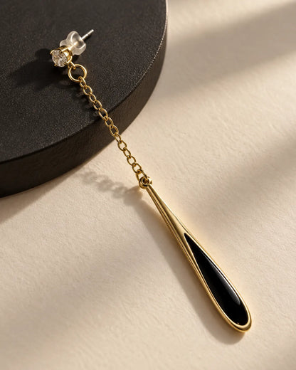Single black teardrop chain earring on a dark surface in sunlight