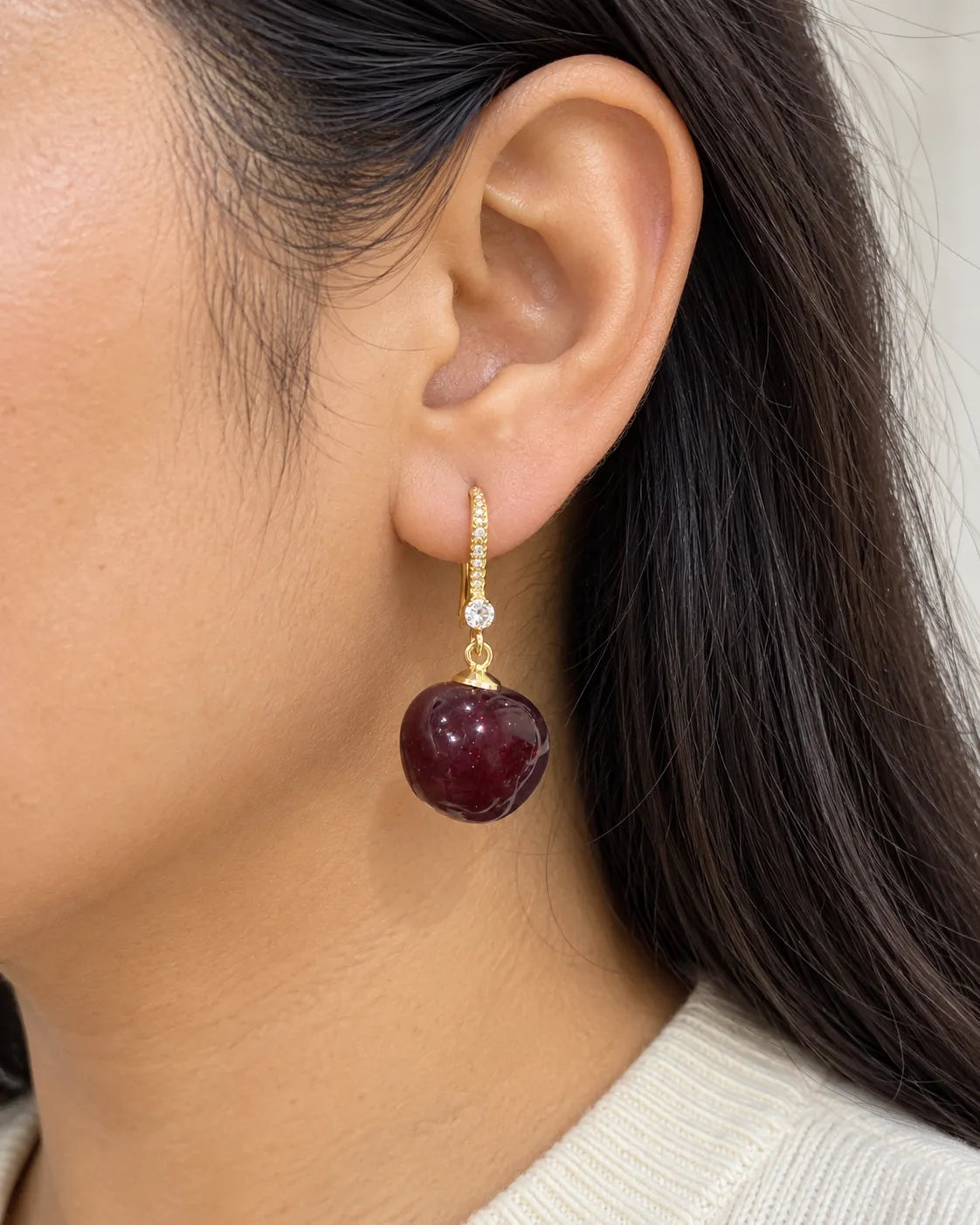 Close-up of a model's ear wearing the burgundy-red cherry drop earring