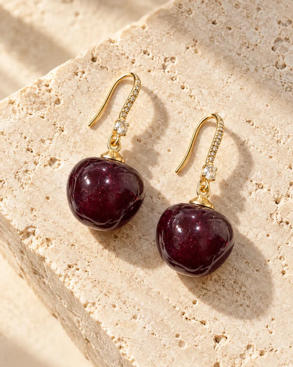 Pair of red cherry drop earrings on a stone surface
