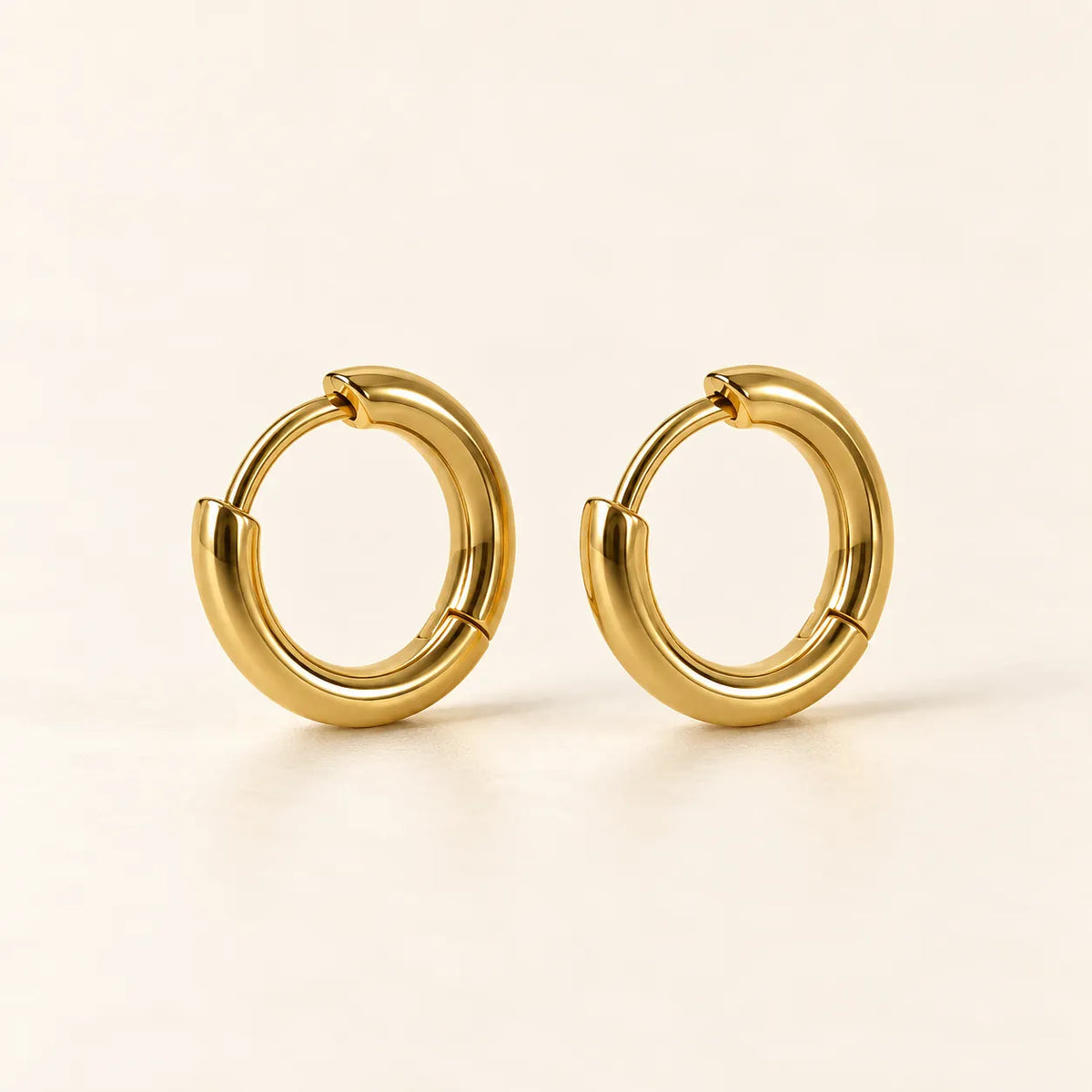 Pair of 18k gold-plated sterling silver huggie hoop earrings on cream