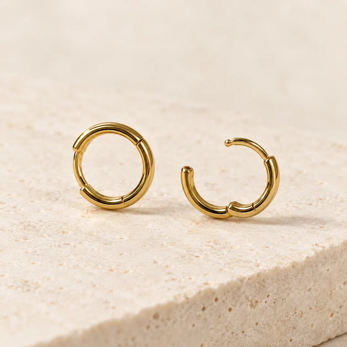 Gold huggie hoops on a stone edge, one closed and one open