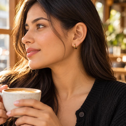 Model holding a coffee cup wearing small gold huggie hoop earrings