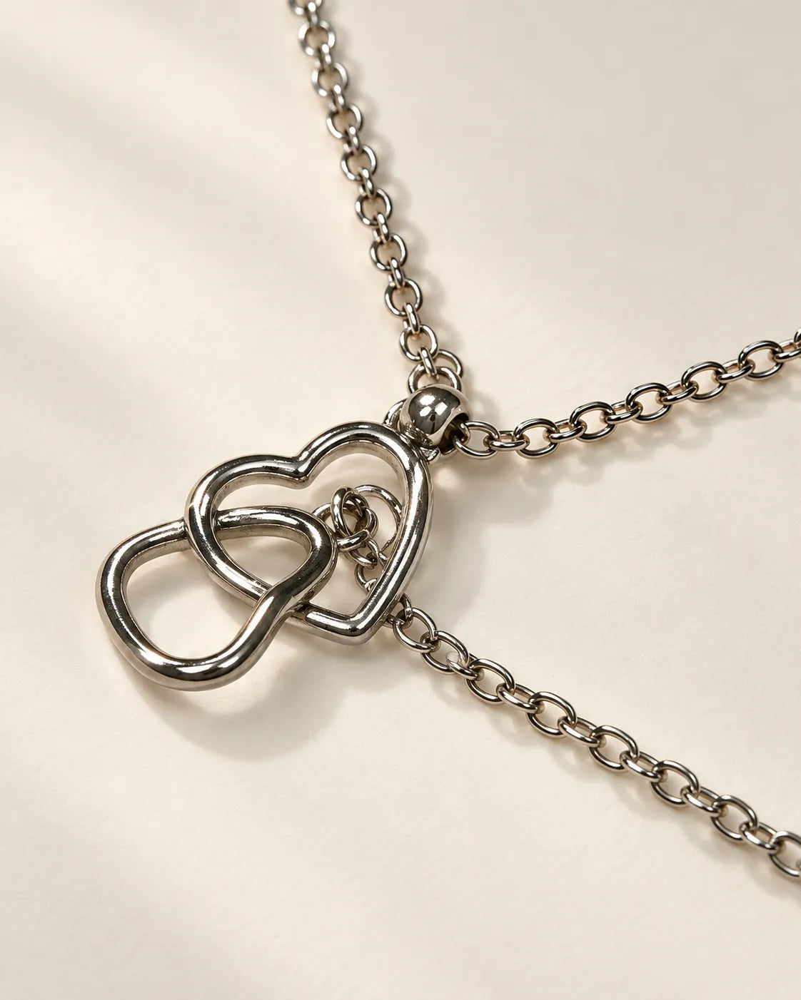Silver-tone interlinked open heart pendant necklace on light linen