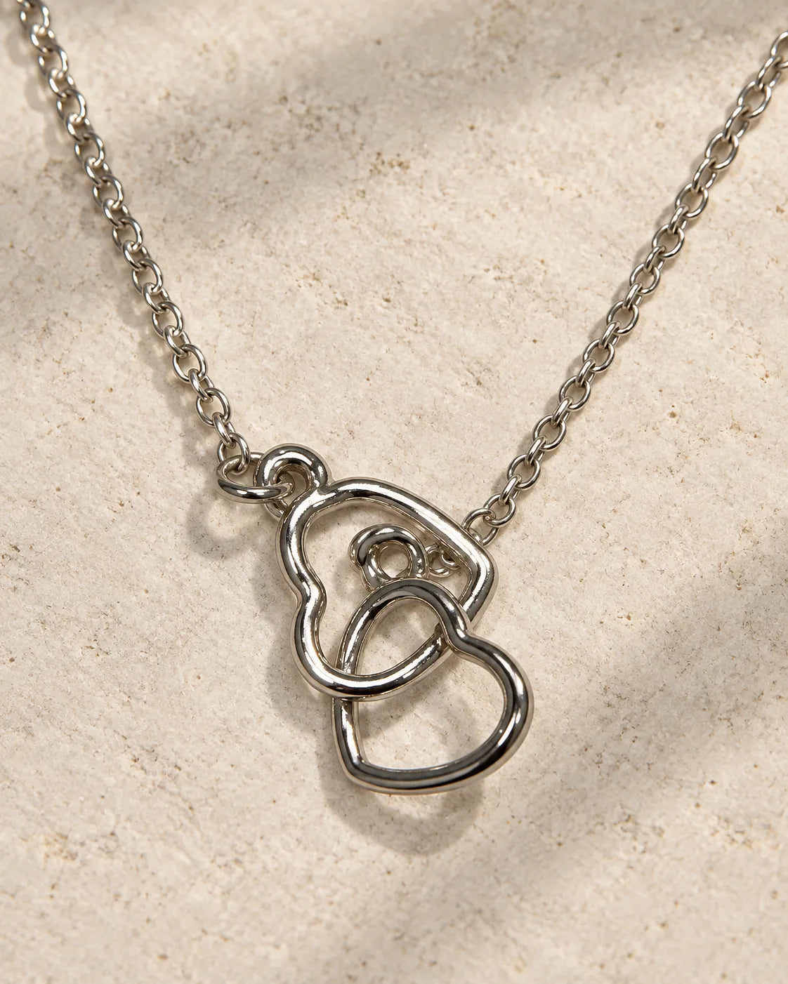Silver double heart necklace hanging against textured linen