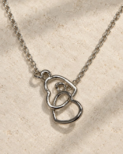Silver double heart necklace hanging against textured linen