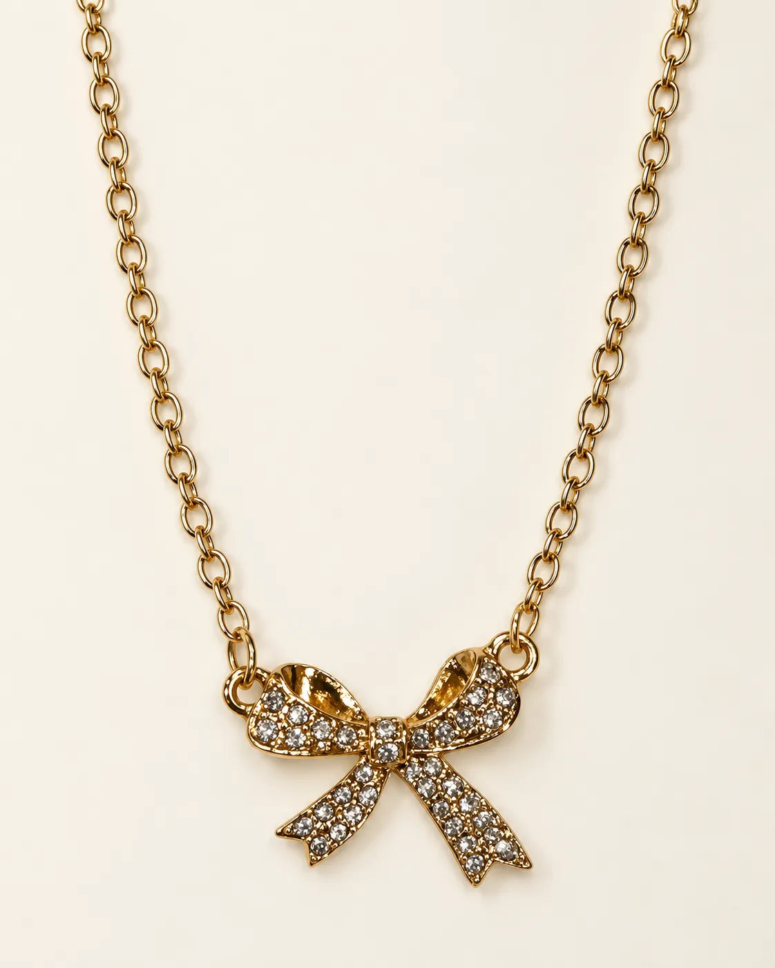 Gold-tone Amélie zircon bow pendant necklace on a cream background