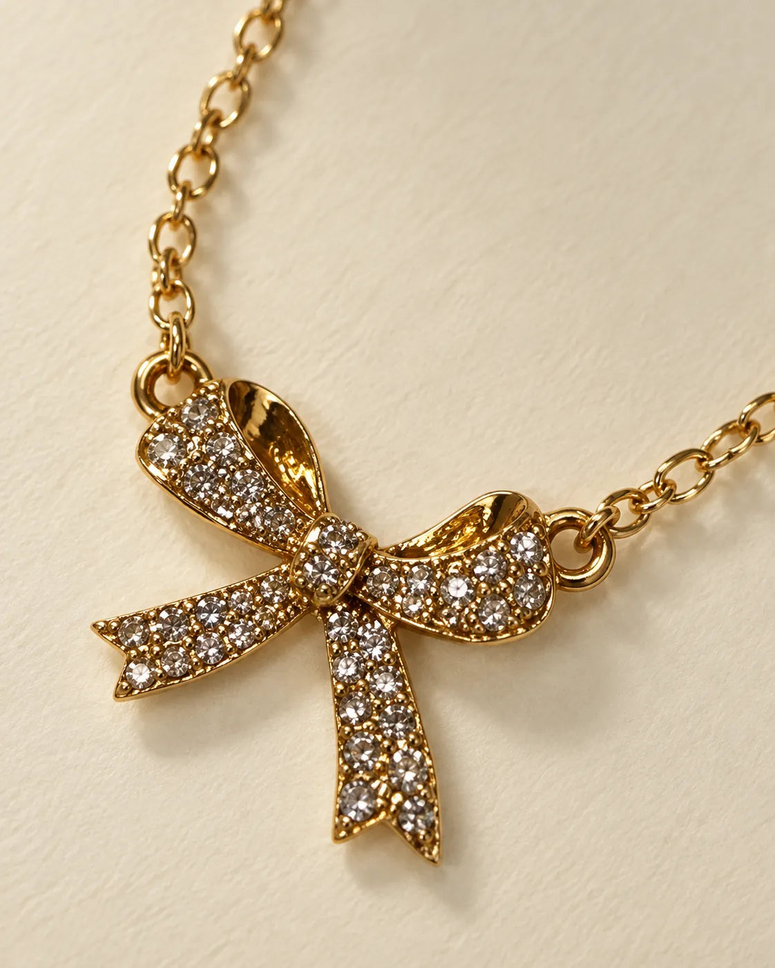 Angled close-up of the gold bow pendant on a cable chain