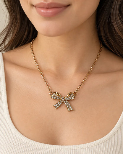 Model in a cream scoop-neck top wearing the gold bow necklace