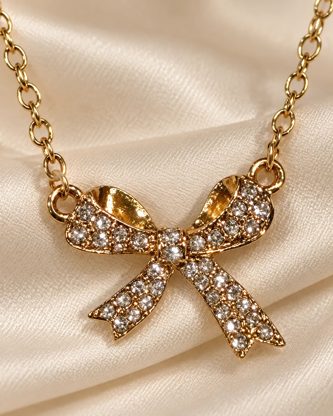 Gold zircon bow necklace resting on champagne satin