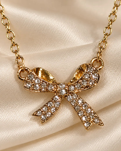 Gold zircon bow necklace resting on champagne satin