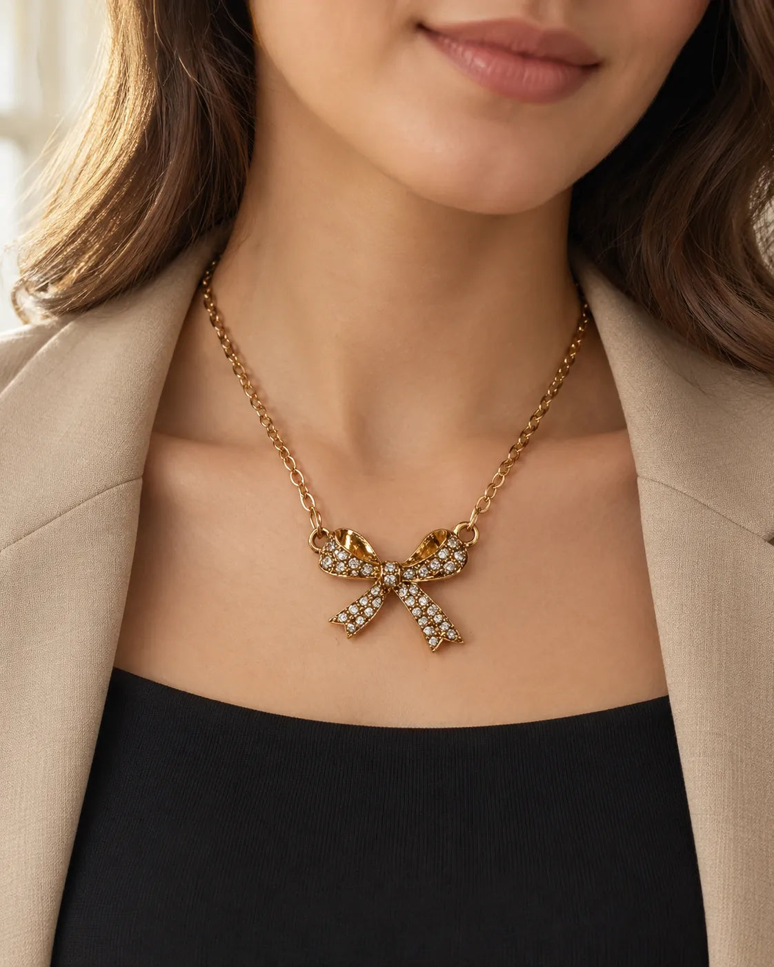 Model in a black top and cream blazer wearing the gold bow pendant
