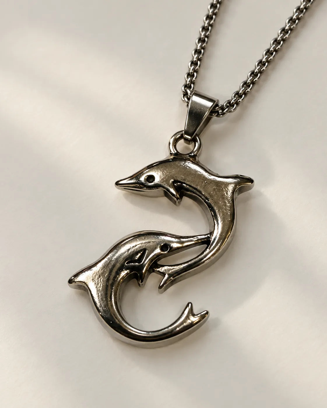 Silver-tone double dolphin pendant necklace on a light grey background
