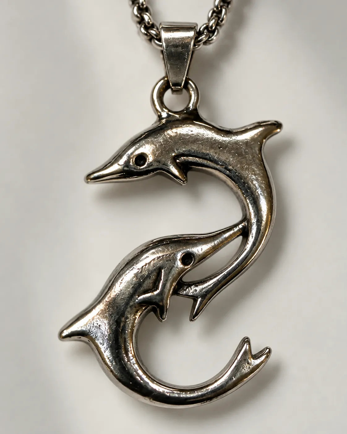 Close-up of the sculpted two-dolphin pendant with antiqued detail