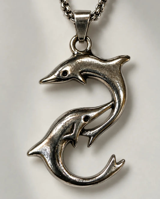 Close-up of the sculpted two-dolphin pendant with antiqued detail
