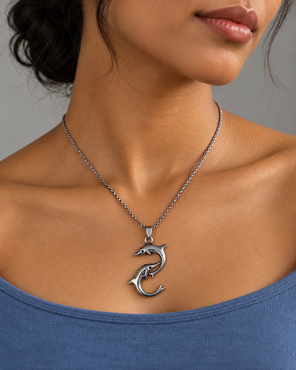 Silver dolphin pendant necklace worn with a blue top, close-up