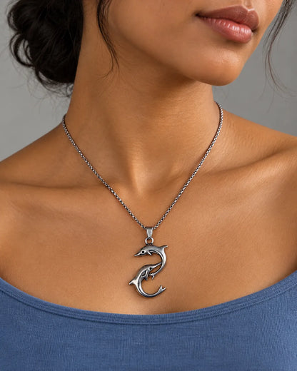 Silver dolphin pendant necklace worn with a blue top, close-up