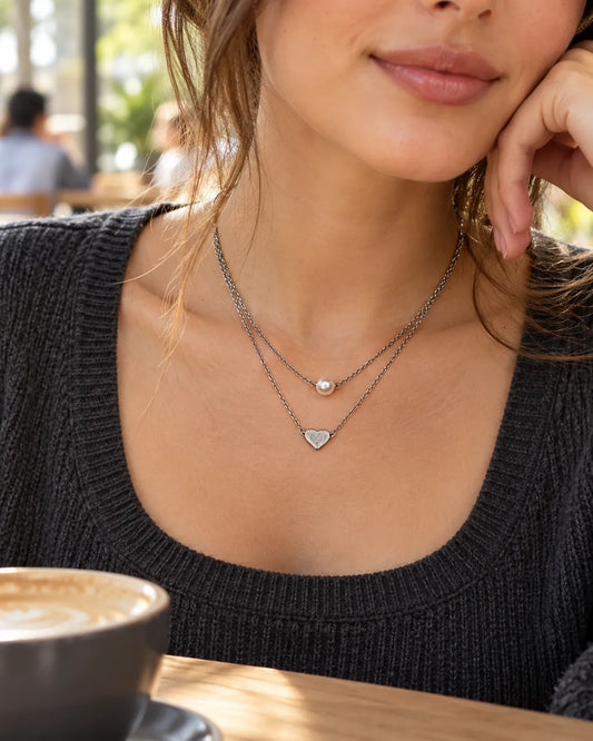 Model in a black knit top wearing the silver pearl and heart necklace