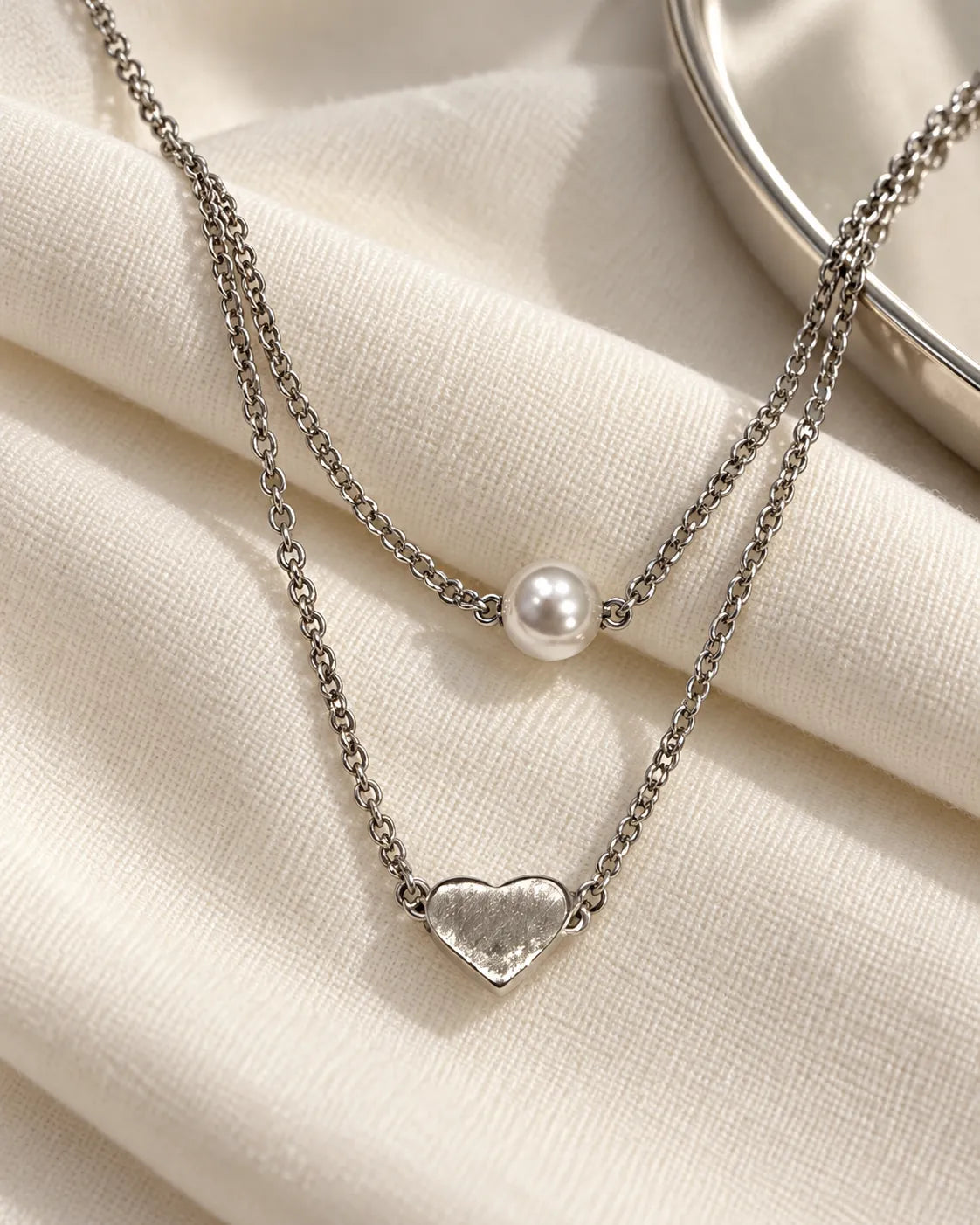 Two-layer silver pearl and heart necklace on cream linen
