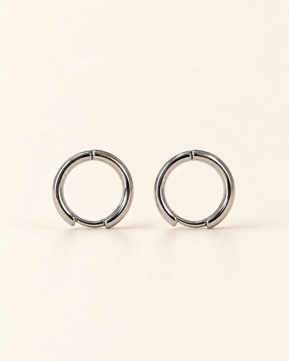 Pair of polished 925 sterling silver huggie hoop earrings on cream