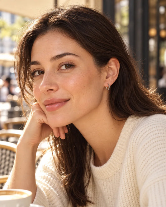 Smiling model at a café wearing small silver huggie hoop earrings