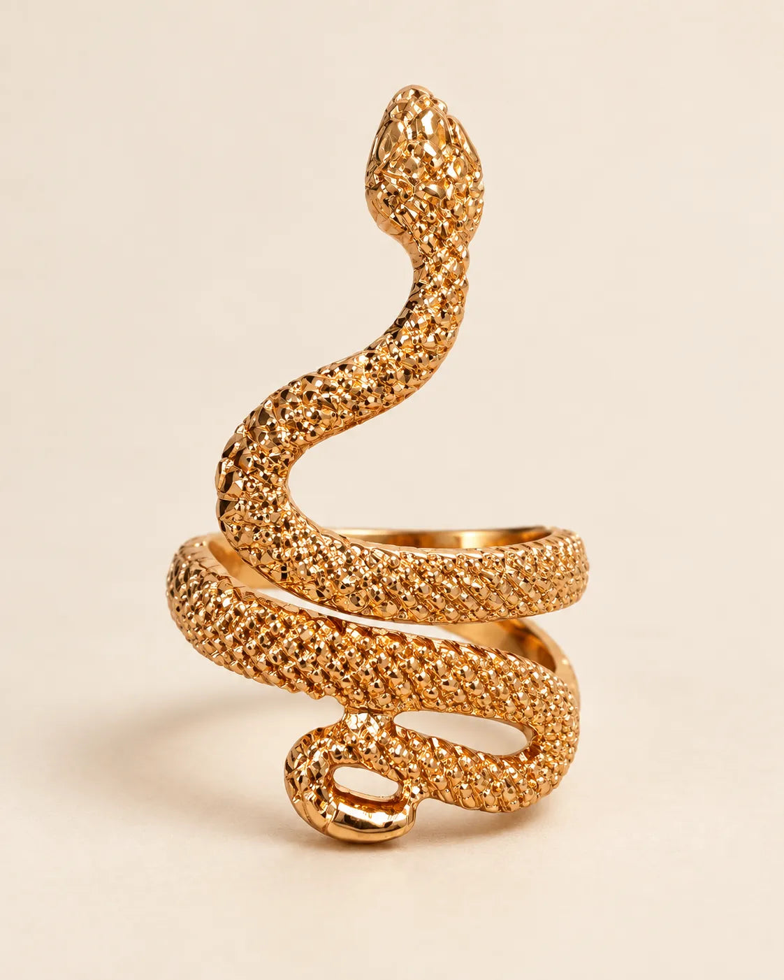 Gold serpent wrap ring with dotted scale texture on a cream background