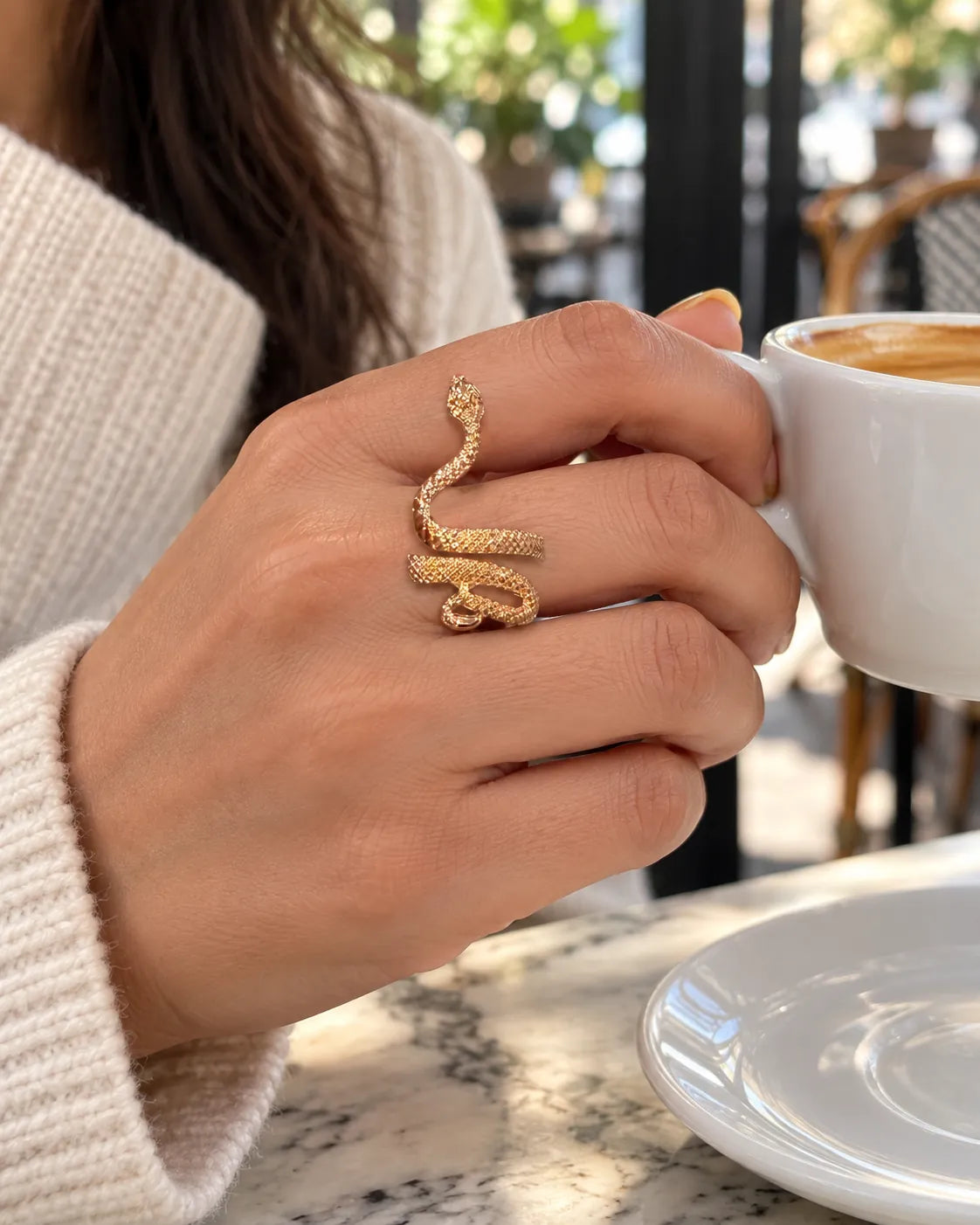Hand holding a coffee cup wearing the gold serpent ring