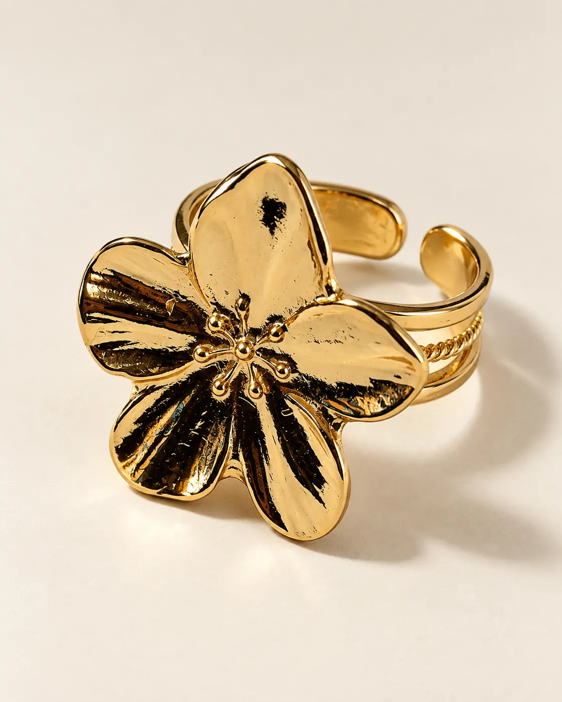 Gold five-petal flower statement ring on a cream background